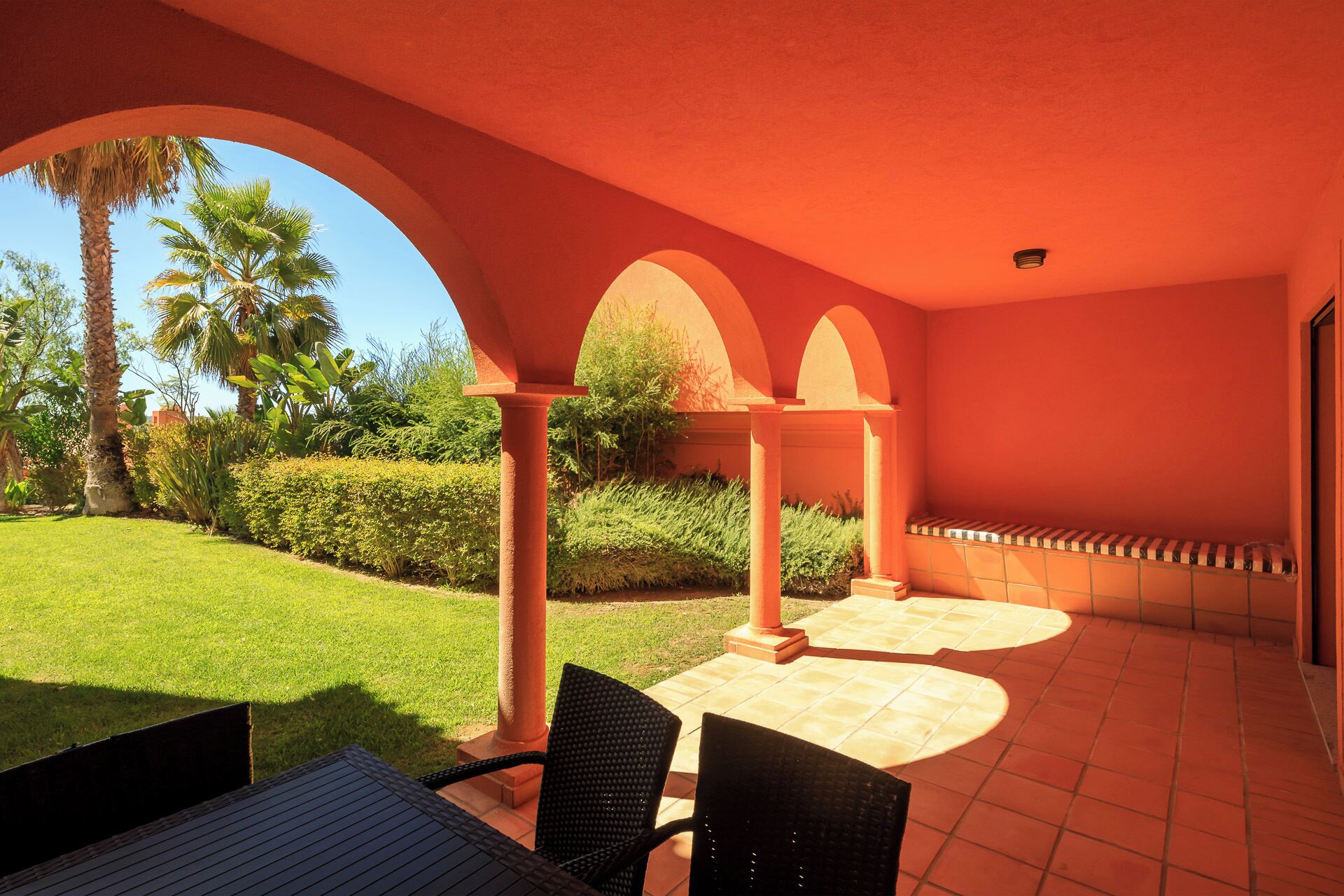 An outdoor patio area with a table and chairs, surrounded by a red wall and arches.
