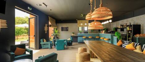 Un interior moderno con una mesa de comedor de madera, sillas tapizadas en verde y una zona de bar.