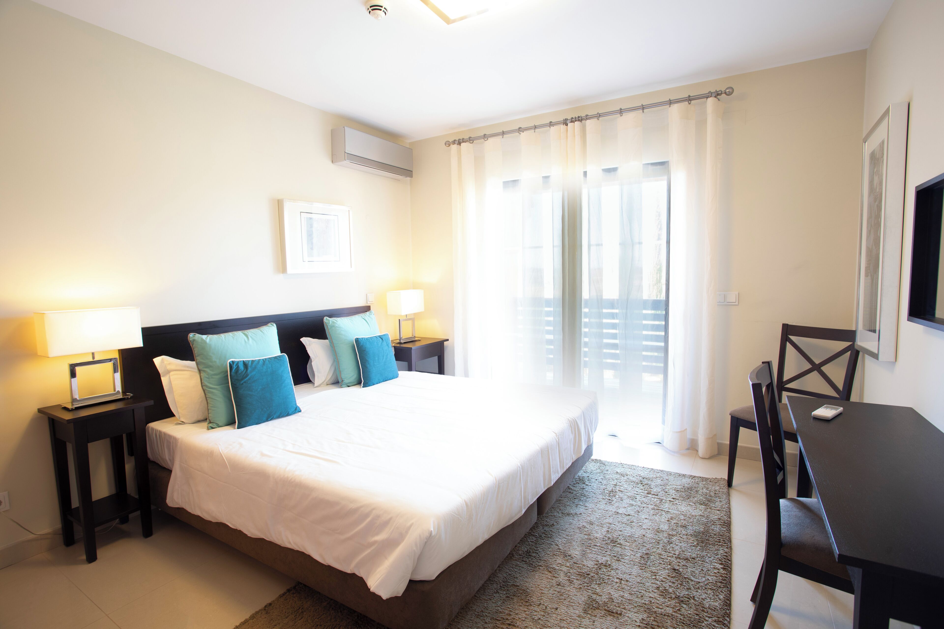 A bedroom with a bed, bedside tables, a desk, and a chair.