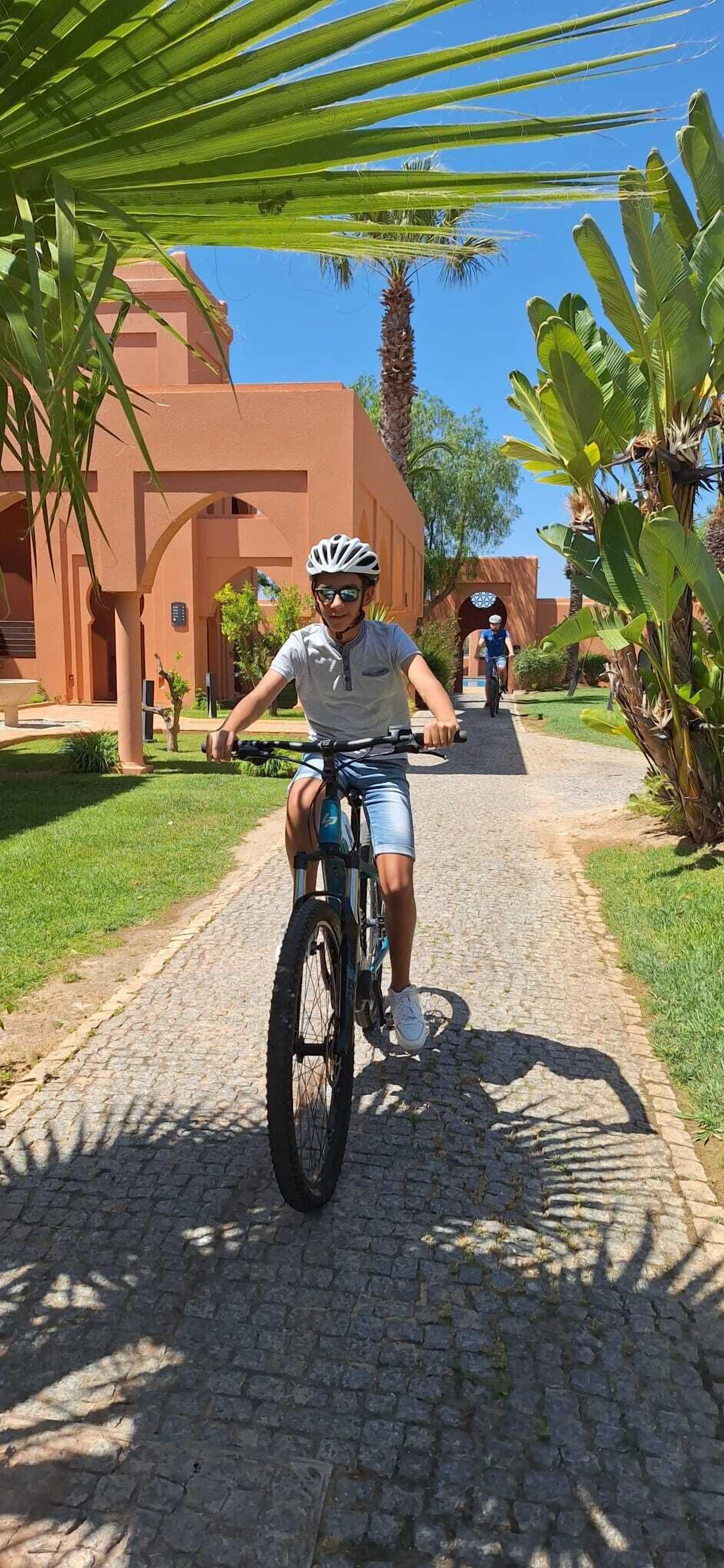 A person riding a bicycle on a cobblestone path with a building in the background.
