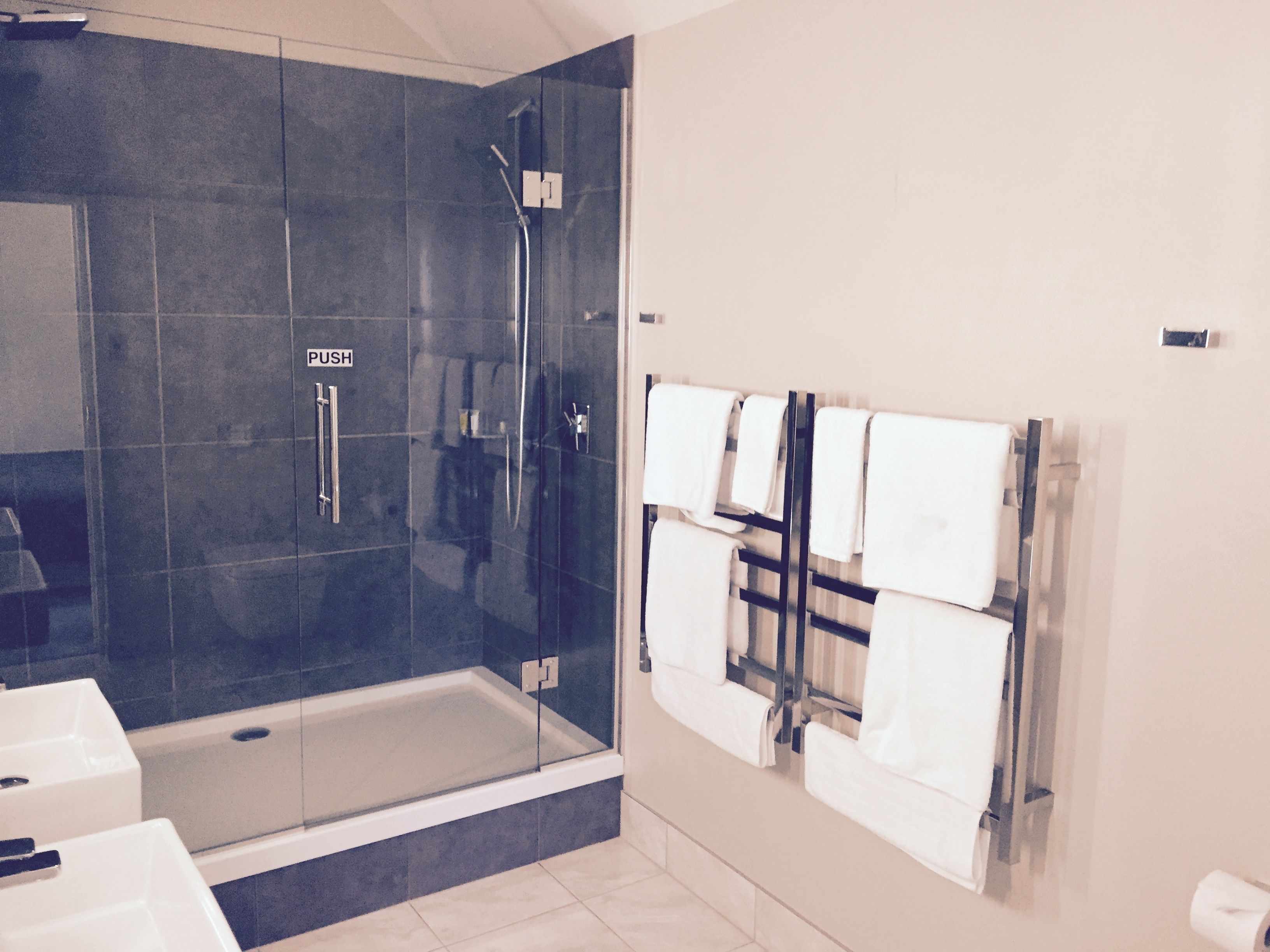 Un baño moderno con ducha envuelta en vidrio, bañera y toallero con varias toallas.