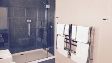 Un baño moderno con ducha envuelta en vidrio, bañera y toallero con varias toallas.