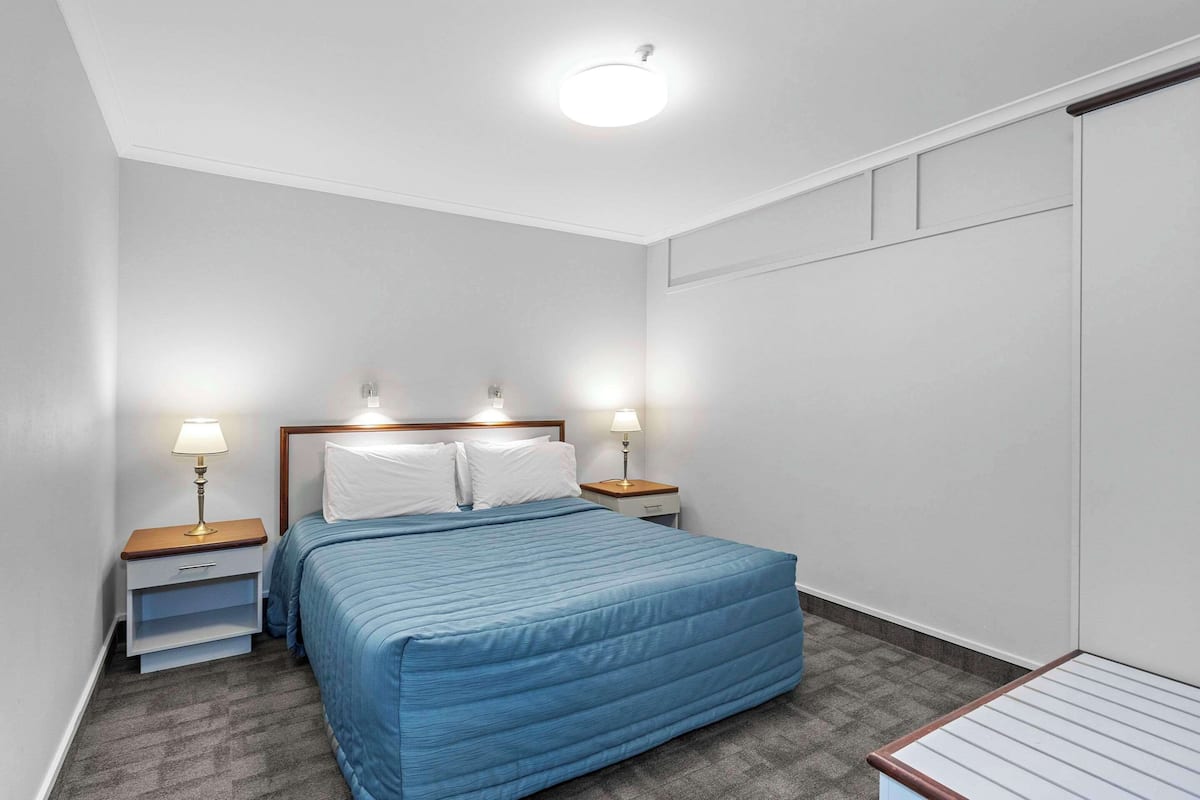 A bedroom with a bed, two bedside tables with lamps, a nightstand, and a wardrobe.