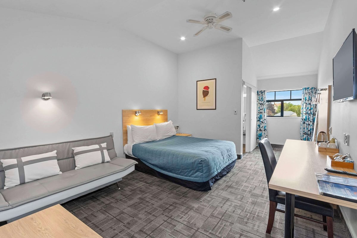 A hotel room with a bed, a sofa, a desk, and a ceiling fan.