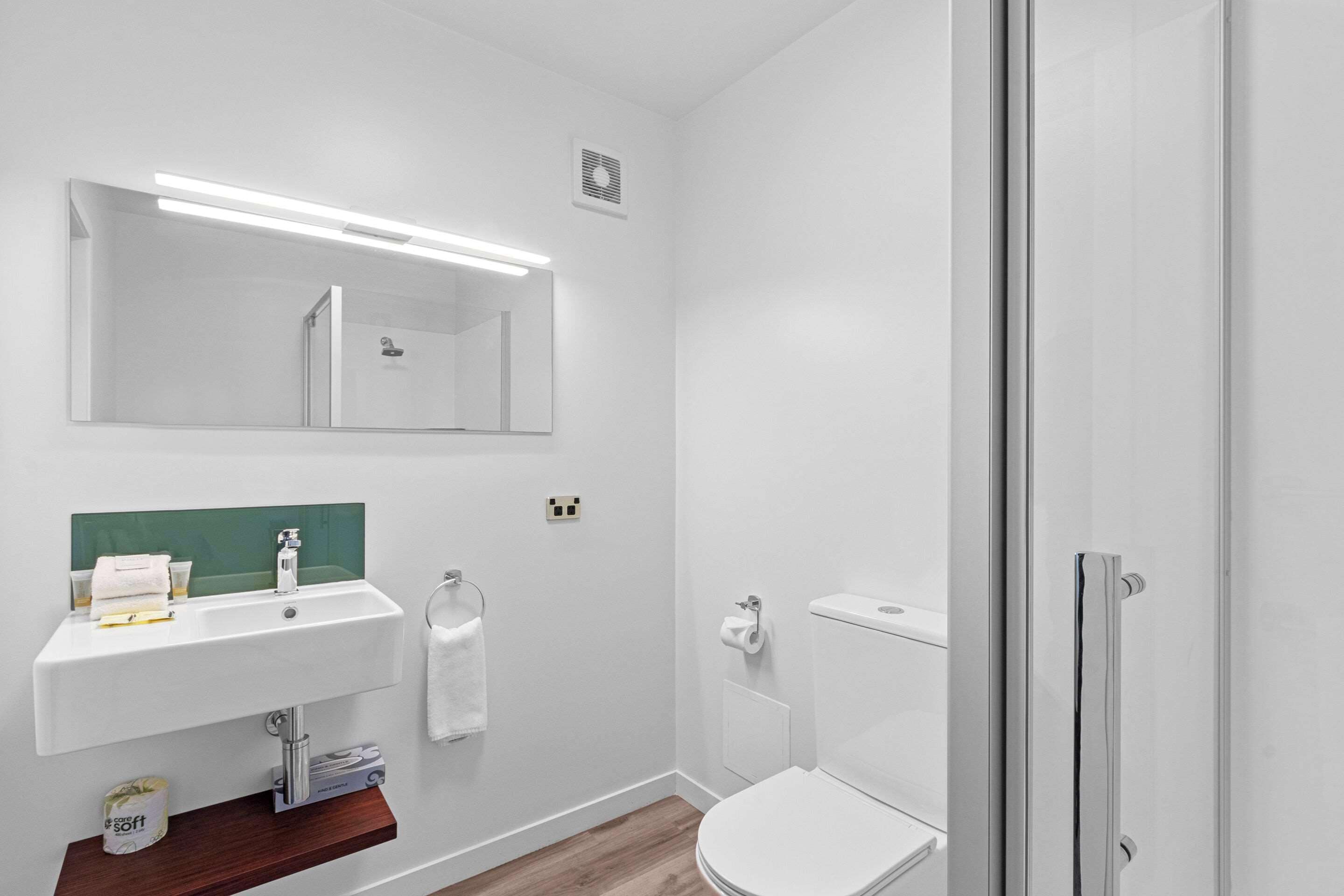 Et moderne badeværelse med hvid vask, spejl og toilet.