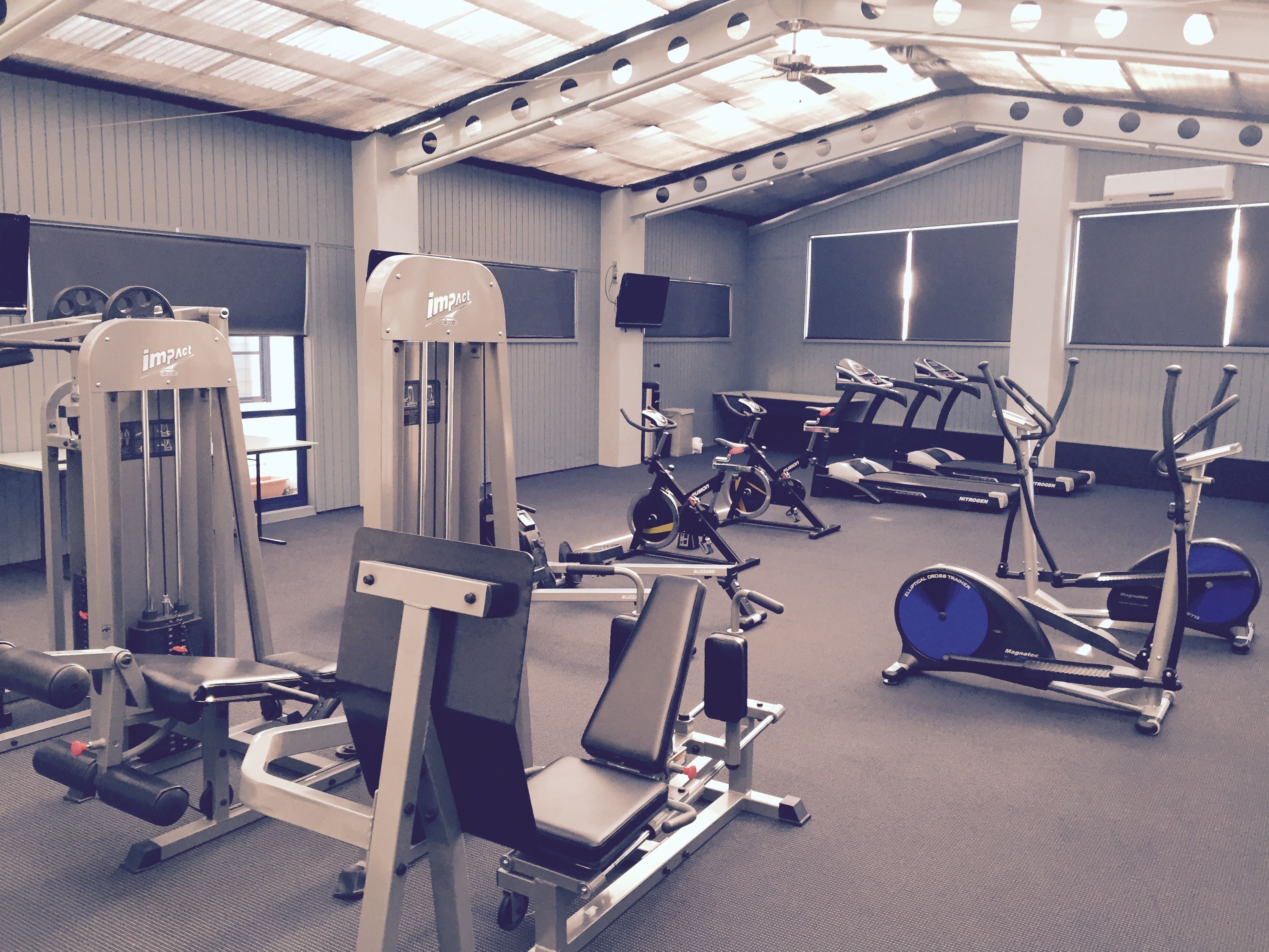 Ein Fitnessstudio mit verschiedenen Trainingsgeräten, darunter Kraftgeräte, Laufbänder und Hantbikes.