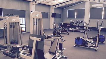 Ein Fitnessstudio mit verschiedenen Trainingsgeräten, darunter Kraftgeräte, Laufbänder und Hantbikes.