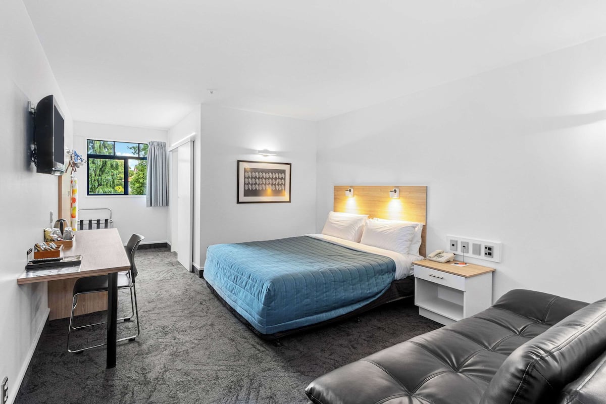A hotel room with a bed, a desk, a chair, a TV, and a window with curtains.