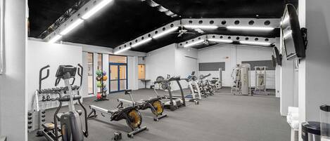 A gym with various exercise machines, a ceiling fan, and a TV mounted on the wall.