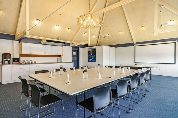 A conference room with a long table, chairs, a projector screen, and a chandelier.
