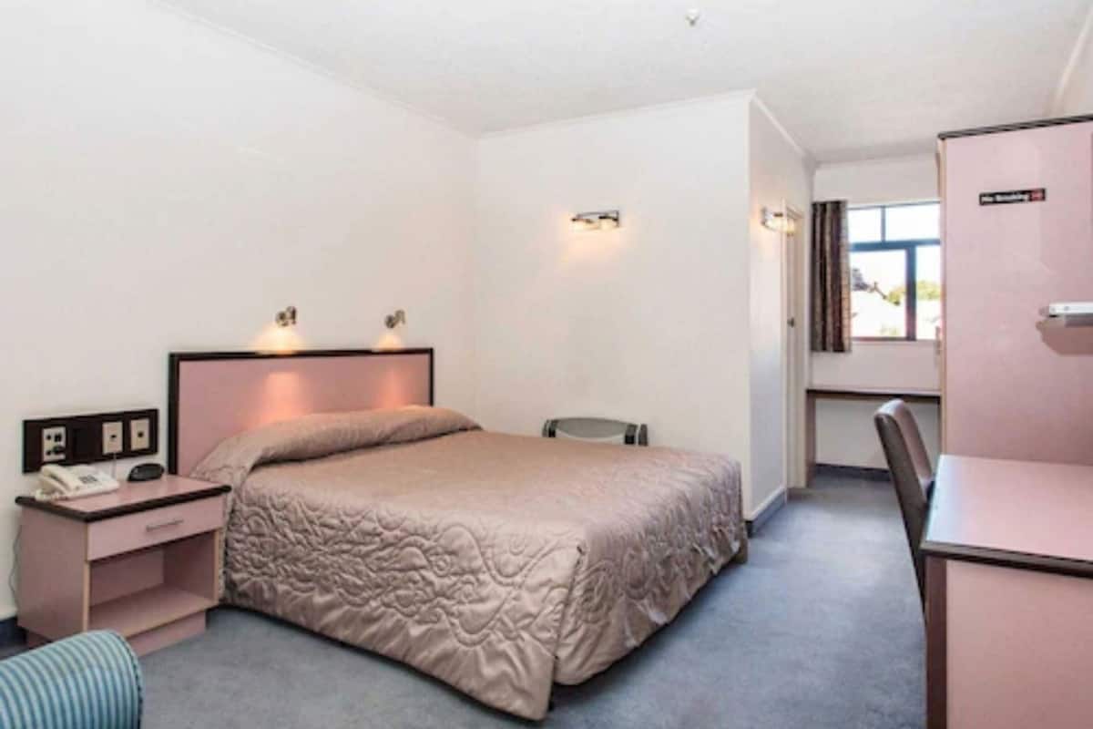 A single bed with a headboard, bedside table with a lamp, a small desk, and a chair.