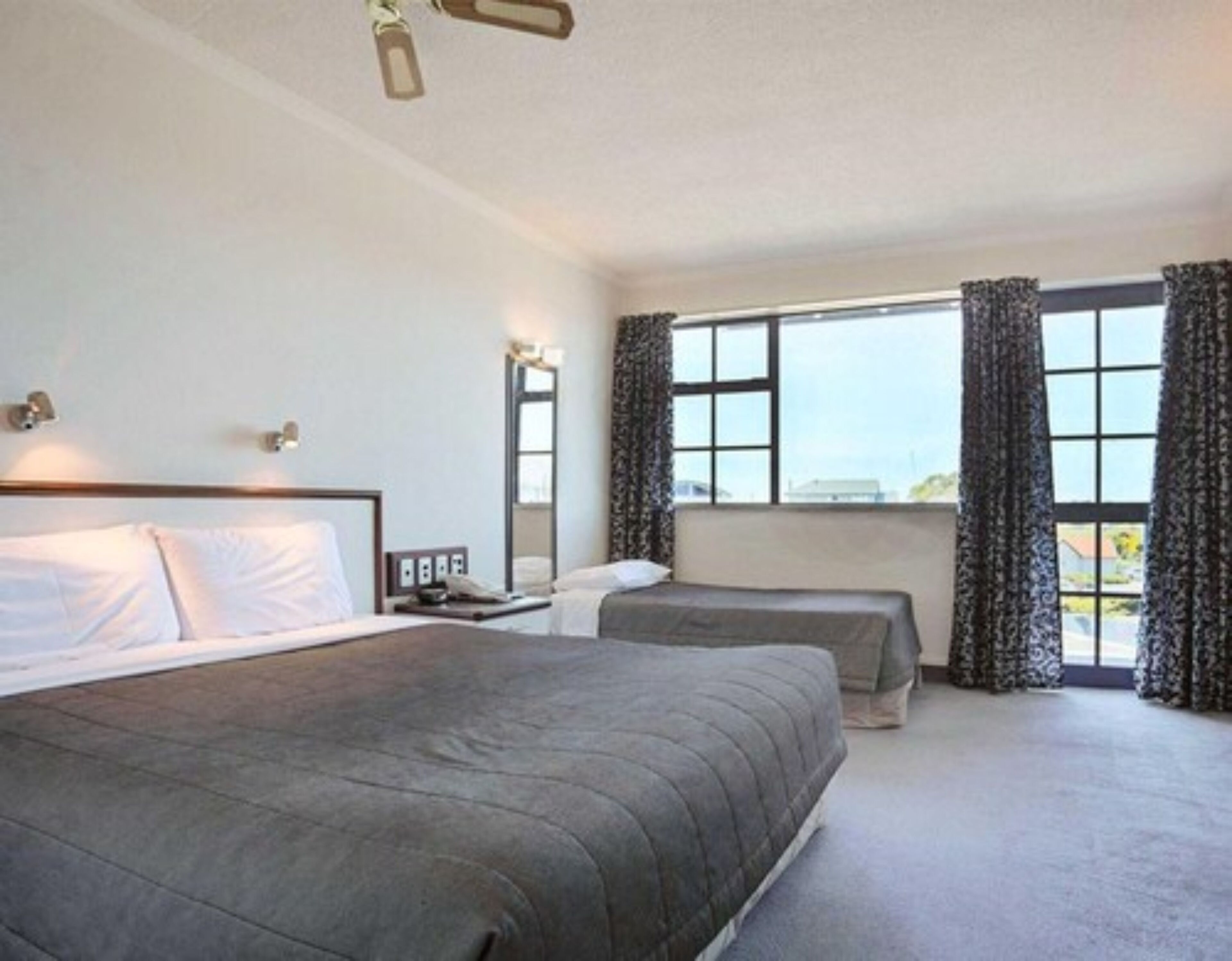 A hotel room with a large bed, a smaller bed, a desk with a lamp, and a window with curtains.