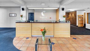 Una zona de recepción con un mostrador de vidrio, un jarrón con flores y un cartel que dice 'Comfort Hotel'.