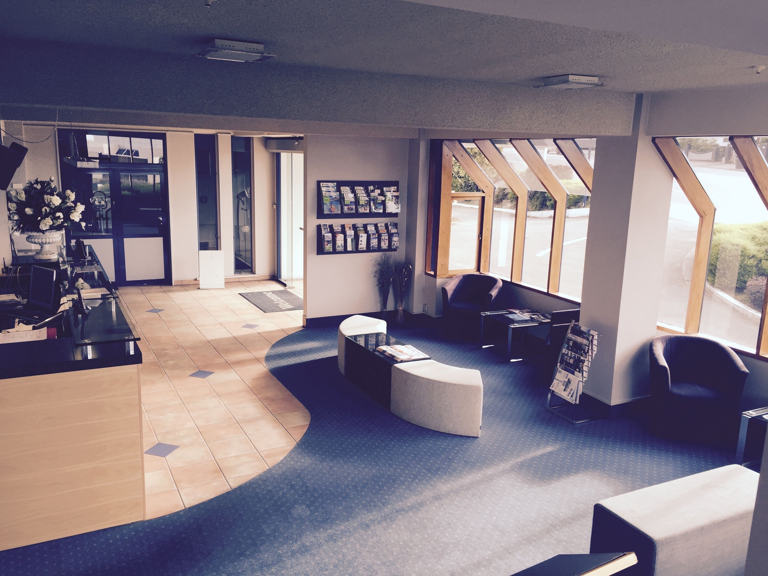 A modern lobby with a curved reception desk, seating area with ottomans, and large windows offering views of the outdoors.