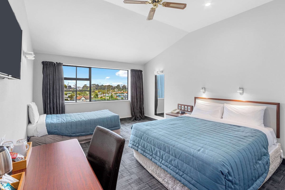 A hotel room with two beds, a desk, a chair, a TV, and a window with a view of a cityscape.