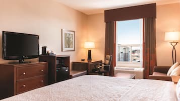Habitación de hotel con una cama grande, un televisor de pantalla plana, un escritorio con una silla, una lámpara de escritorio y una ventana con cortinas.