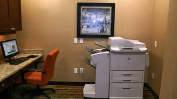 A hotel room with a desk, computer, printer, and an orange chair.