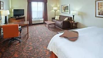 Habitación de hotel con cama, escritorio con silla, sofá, televisor y ventana con cortinas.