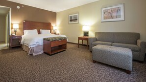 A hotel room with a bed, a sofa, a small table, and two lamps.