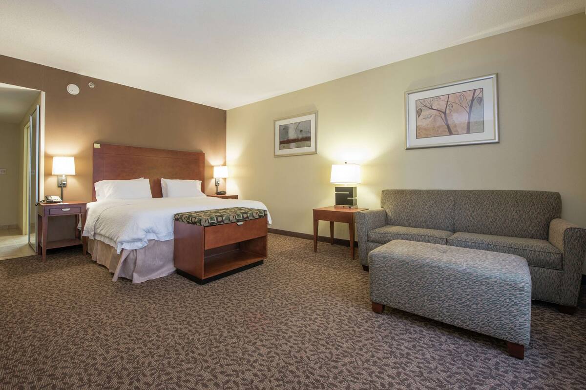 A hotel room with a bed, a sofa, a small table, and two lamps.