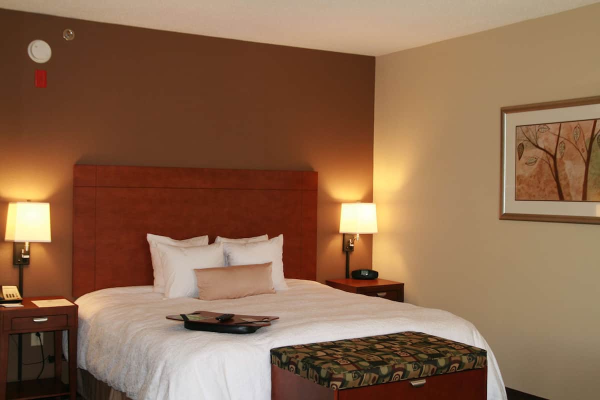A hotel room with a large bed, two bedside lamps, a nightstand, a telephone, and a framed picture on the wall.
