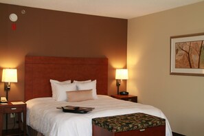 A hotel room with a large bed, two bedside lamps, a nightstand, a telephone, and a framed picture on the wall.