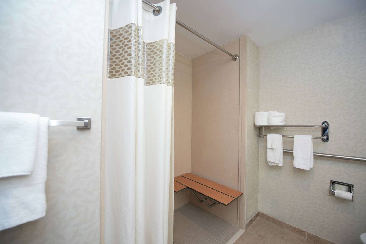 A modern bathroom with a shower, bench, towel rack, and toilet paper holder.