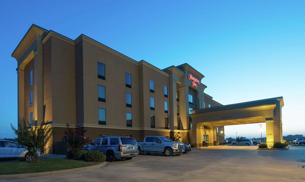 A Hampton Inn hotel with a modern design, featuring a large parking lot and a clear sky.