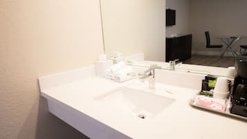 A hotel bathroom with a white sink, a mirror, a towel dispenser, and toiletries.