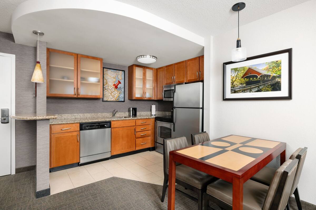 A modern kitchen with wooden cabinets, stainless steel appliances, and a dining area with a table and chairs.