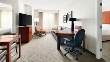 Habitación de hotel con cama, escritorio, silla, televisor, sofá y una pequeña mesa.