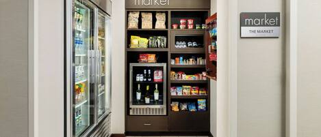 Interior de un supermercado con secciones refrigeradas, estantes llenos de snacks y bebidas, y un letrero que indica la sección de mercado.