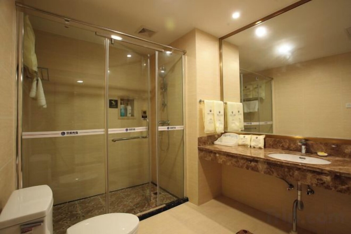 A hotel bathroom with a glass shower enclosure, a toilet, a sink with a marble countertop, and a large mirror.