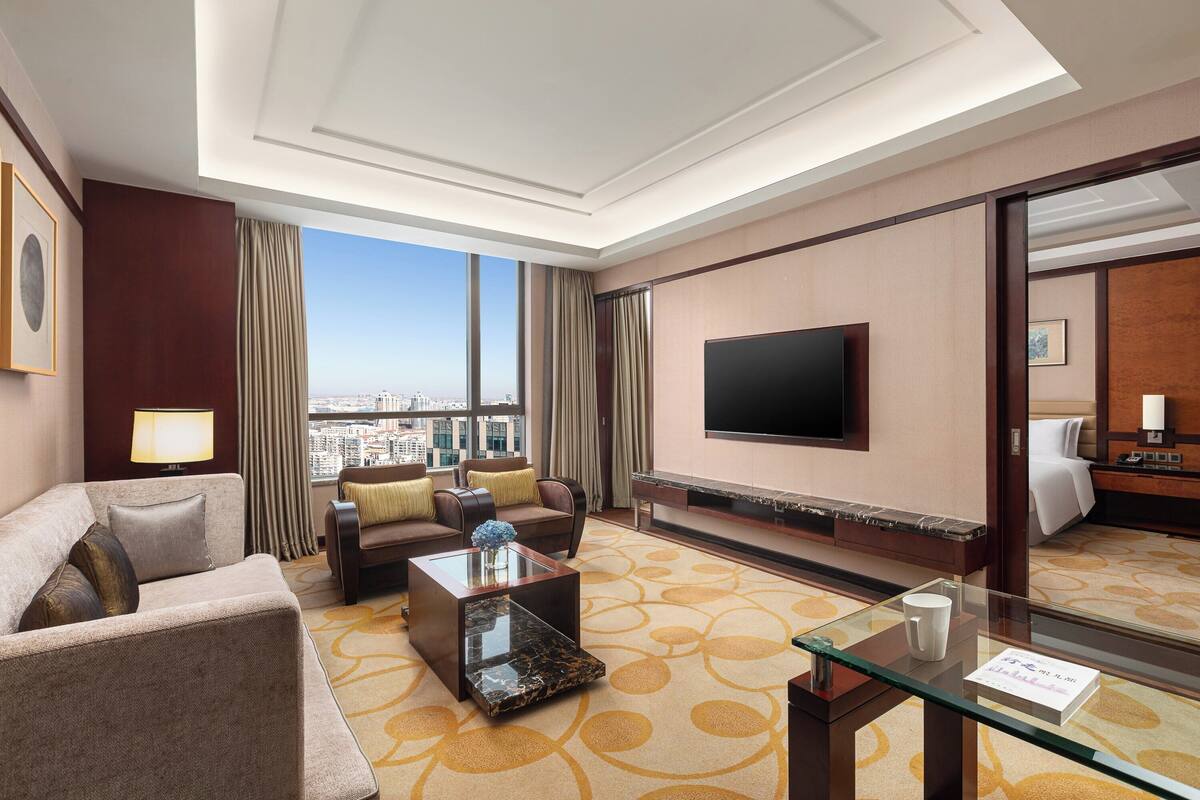 Ein Hotelzimmer mit großem Fenster, einem Flachbildfernseher, einer Couch, einem Couchtisch und einem Bett.