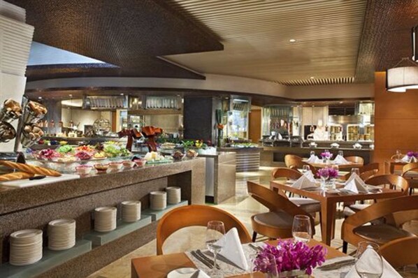 Un restaurante moderno con barra libre, mesas de madera y una cocina al fondo.