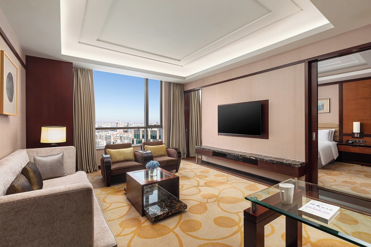 Una habitación de hotel con un ventanal grande, un televisor de pantalla plana, un sofá, una mesa de centro y una cama.