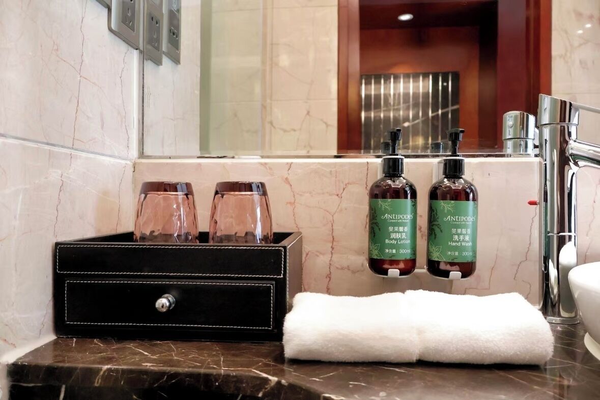 A bathroom with a marble sink, two hand soap bottles, a towel, and a black toiletry box.