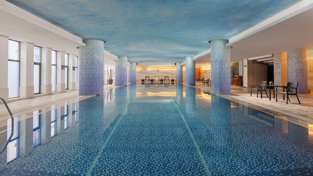 Una amplia piscina cubierta con suelo y techo de azulejos, rodeada de columnas y zonas de estar.