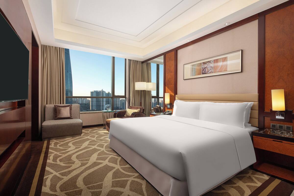 Ein Hotelzimmer mit einem großen Bett, einem Schreibtisch, einem Sessel und Blick auf die Stadt.