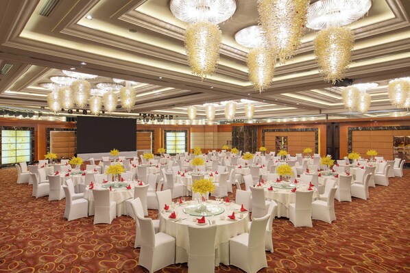 Un salón de banquetes con mesas redondas, sillas blancas y candelabros.