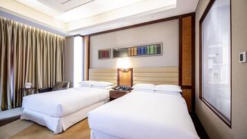 A hotel room with two beds, a desk, a chair, a lamp, and a window with blinds.
