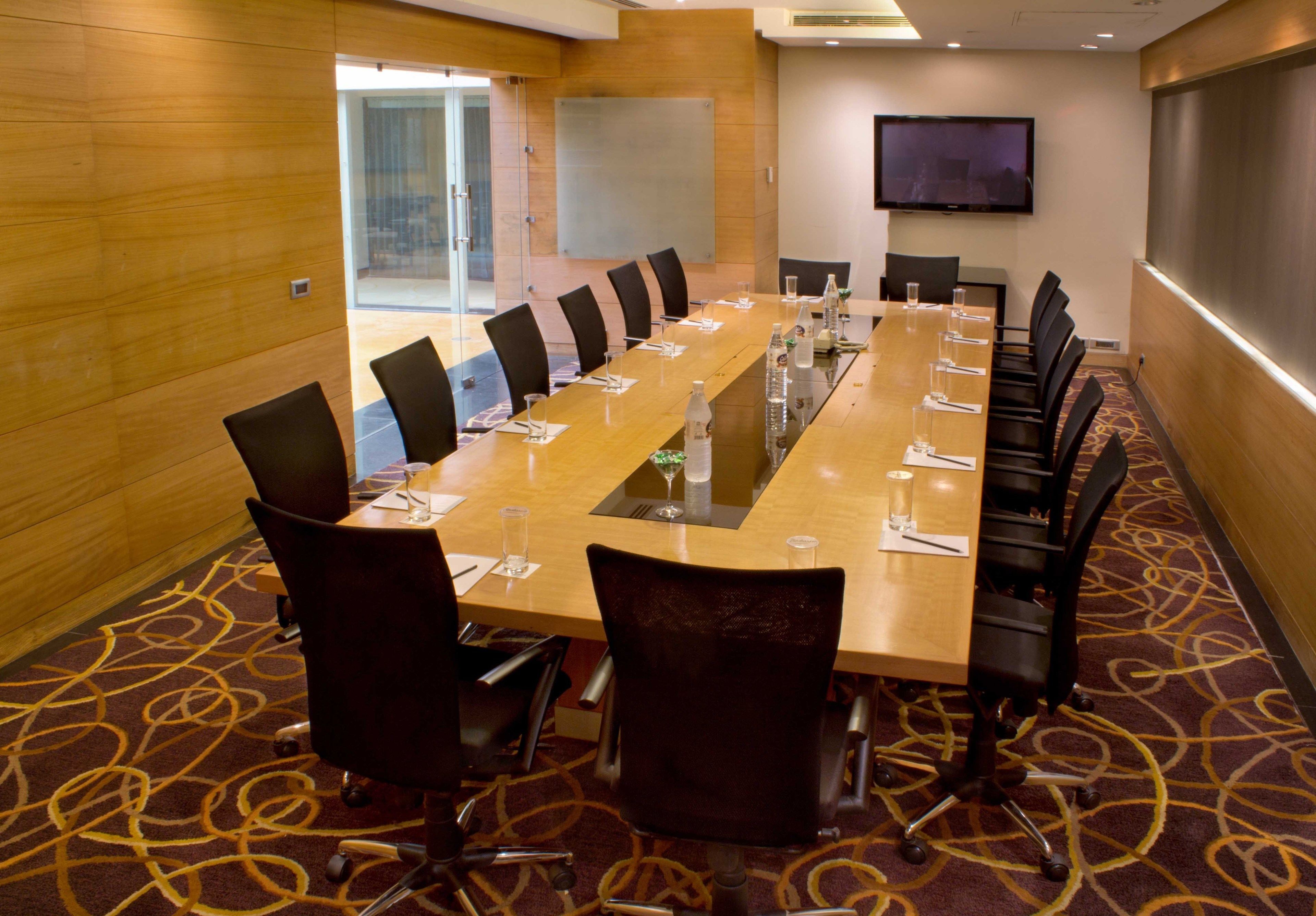 A conference room with a long table, chairs, a TV screen, and a carpeted floor.