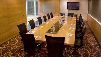 A conference room with a long table, chairs, a TV screen, and a carpeted floor.
