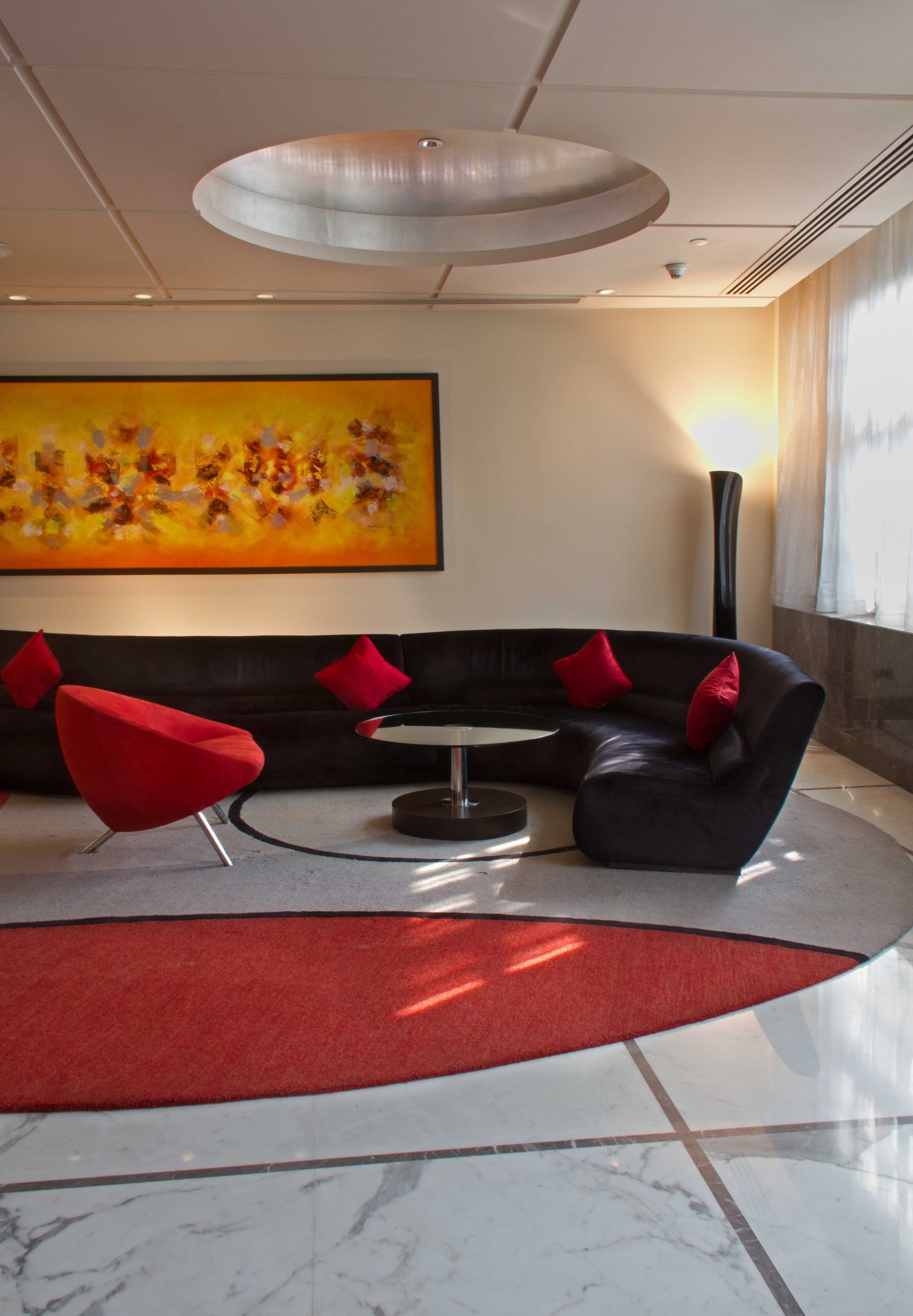 A modern lobby with a black leather sofa, red accent pillows, a round table, and a large abstract painting on the wall.