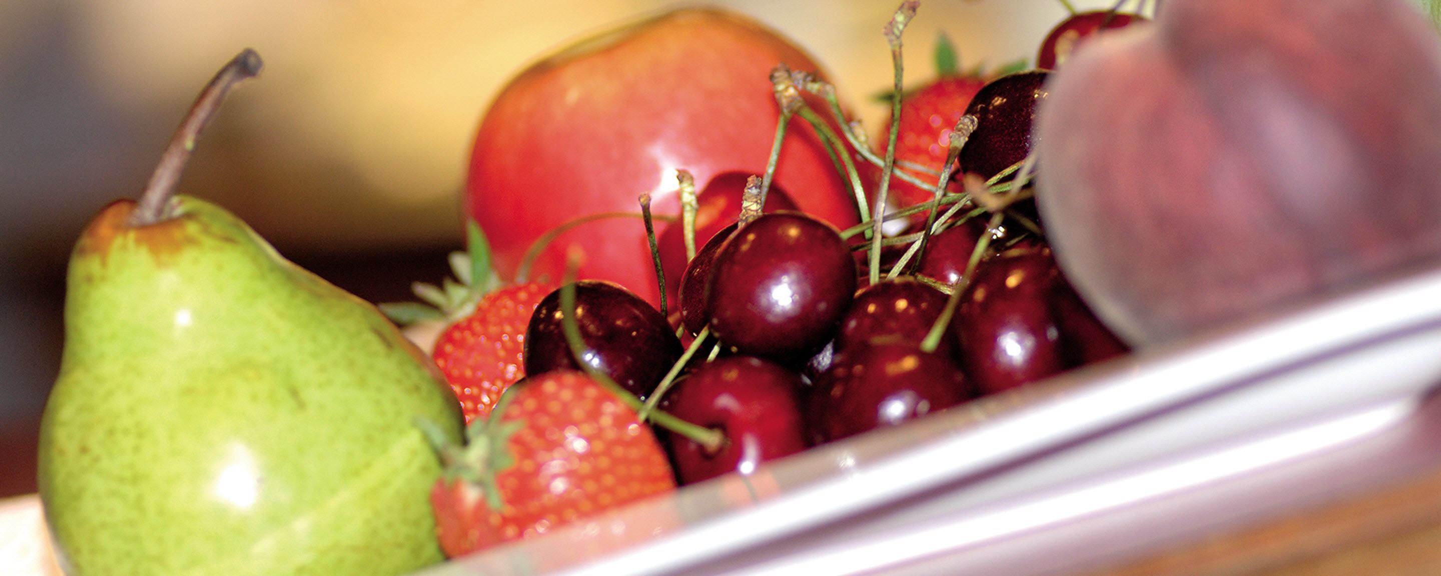 A close-up of a fruit bowl containing a pear, strawberries, and cherries.