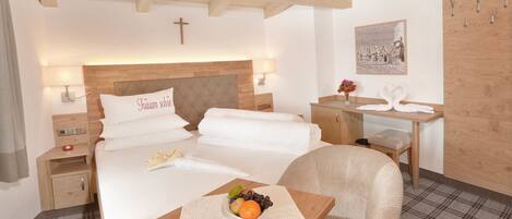 Habitación de hotel con cama, mesitas de noche, escritorio, silla y una cruz en la pared.