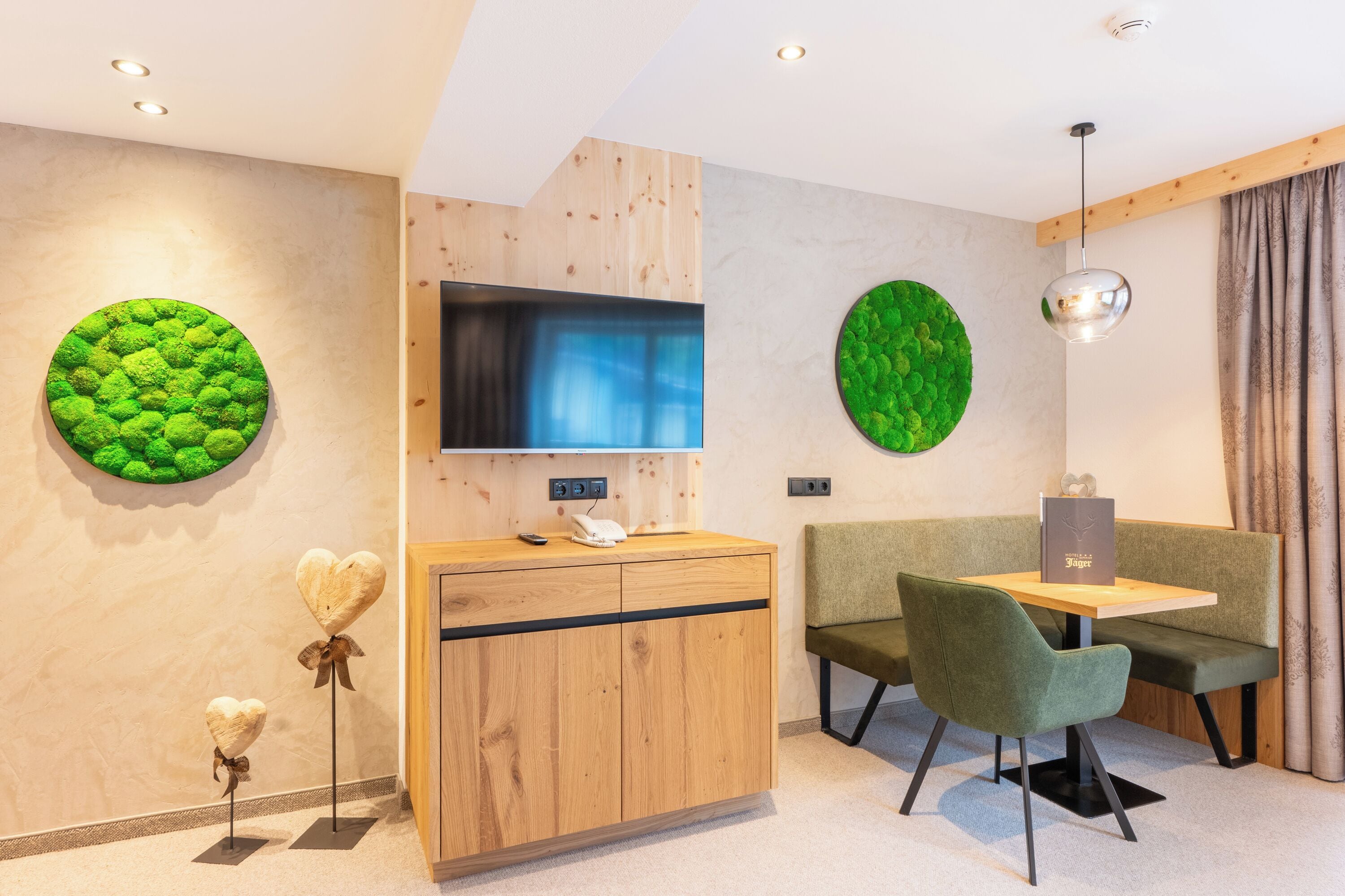 Una habitación de hotel moderna con un mostrador de recepción de madera, un televisor de pantalla plana, un adorno de pared verde, un sofá verde y una mesa de comedor con sillas.