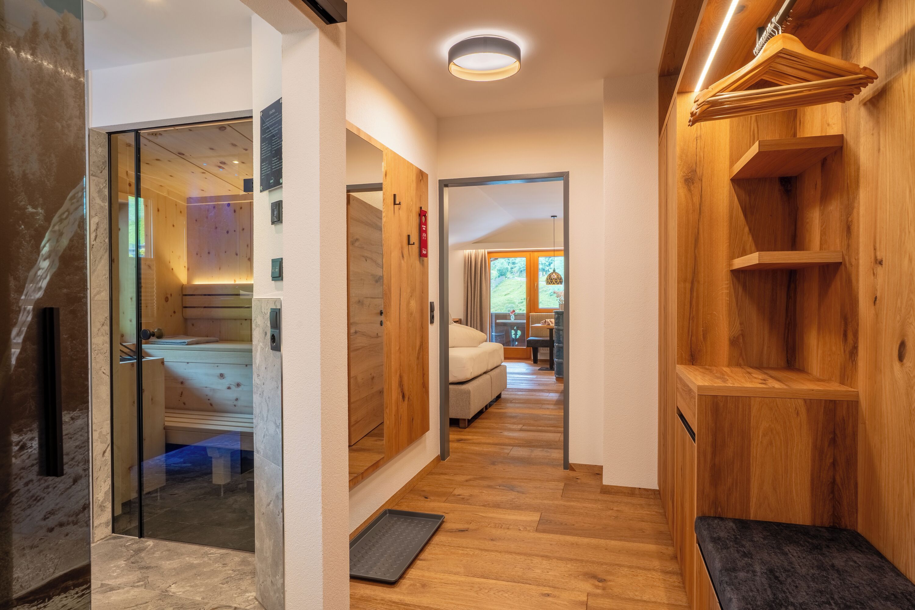 Un pasillo con suelo de madera, un banco, una zona de sauna y una estantería de madera.