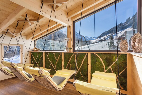 Une pièce avec des poutres en bois, de grandes fenêtres et deux fauteuils suspendus dotés de coussins.