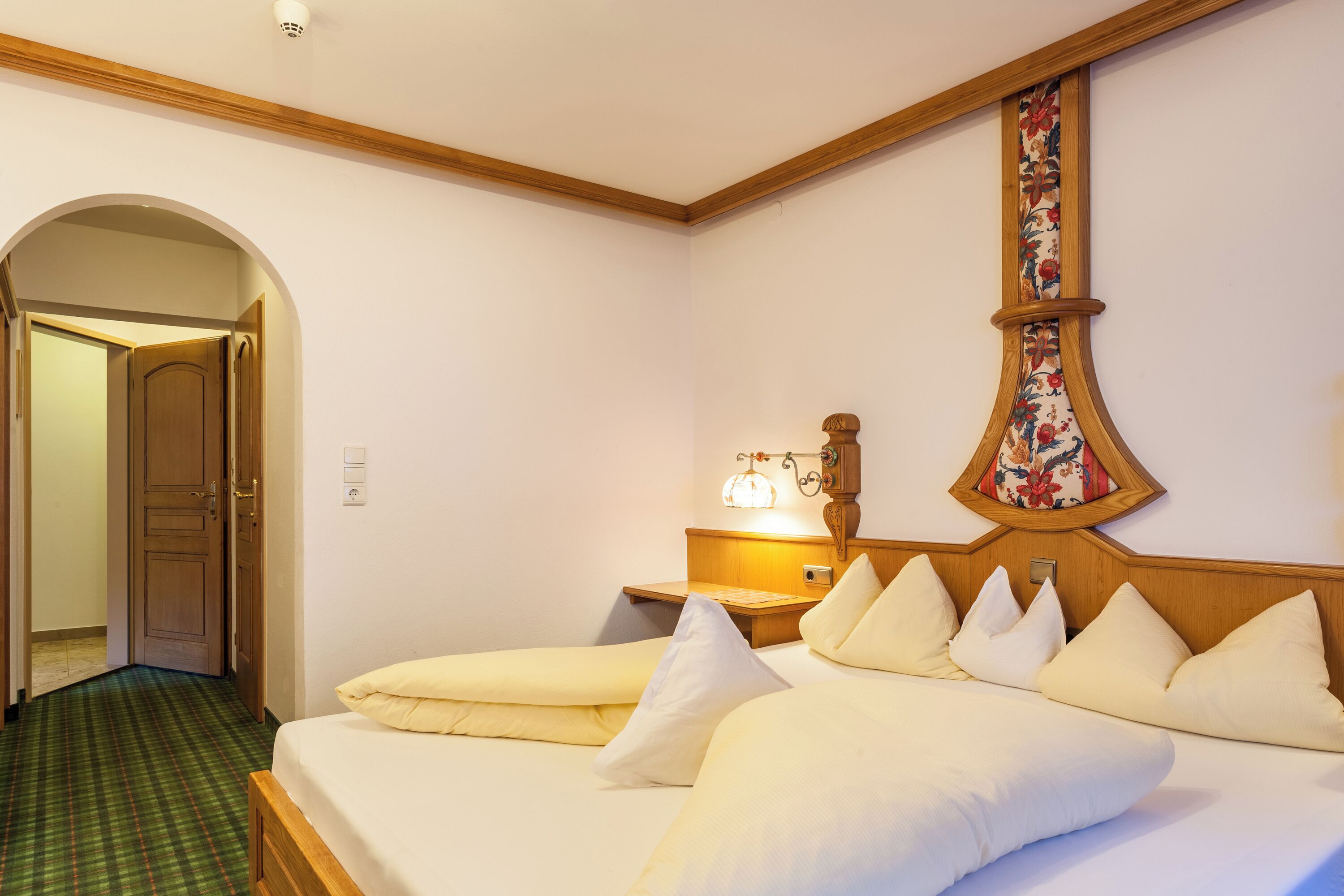 A hotel room with a bed, a nightstand, a lamp, and a floral-patterned wall decoration.